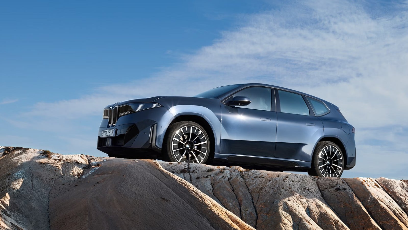 BMW iX3 50 xDrive azul estacionado sobre rochas, visto de lado
