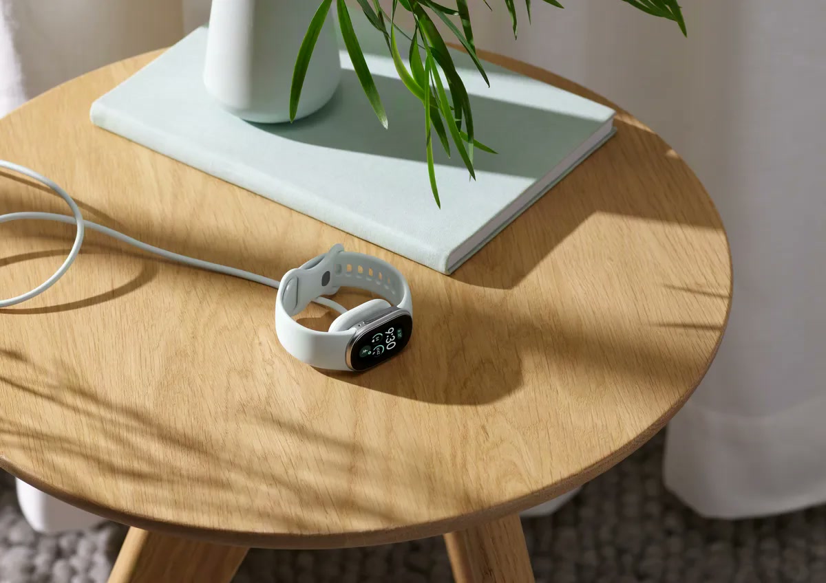 Fitbit Edge branca carregando sobre uma mesa de madeira