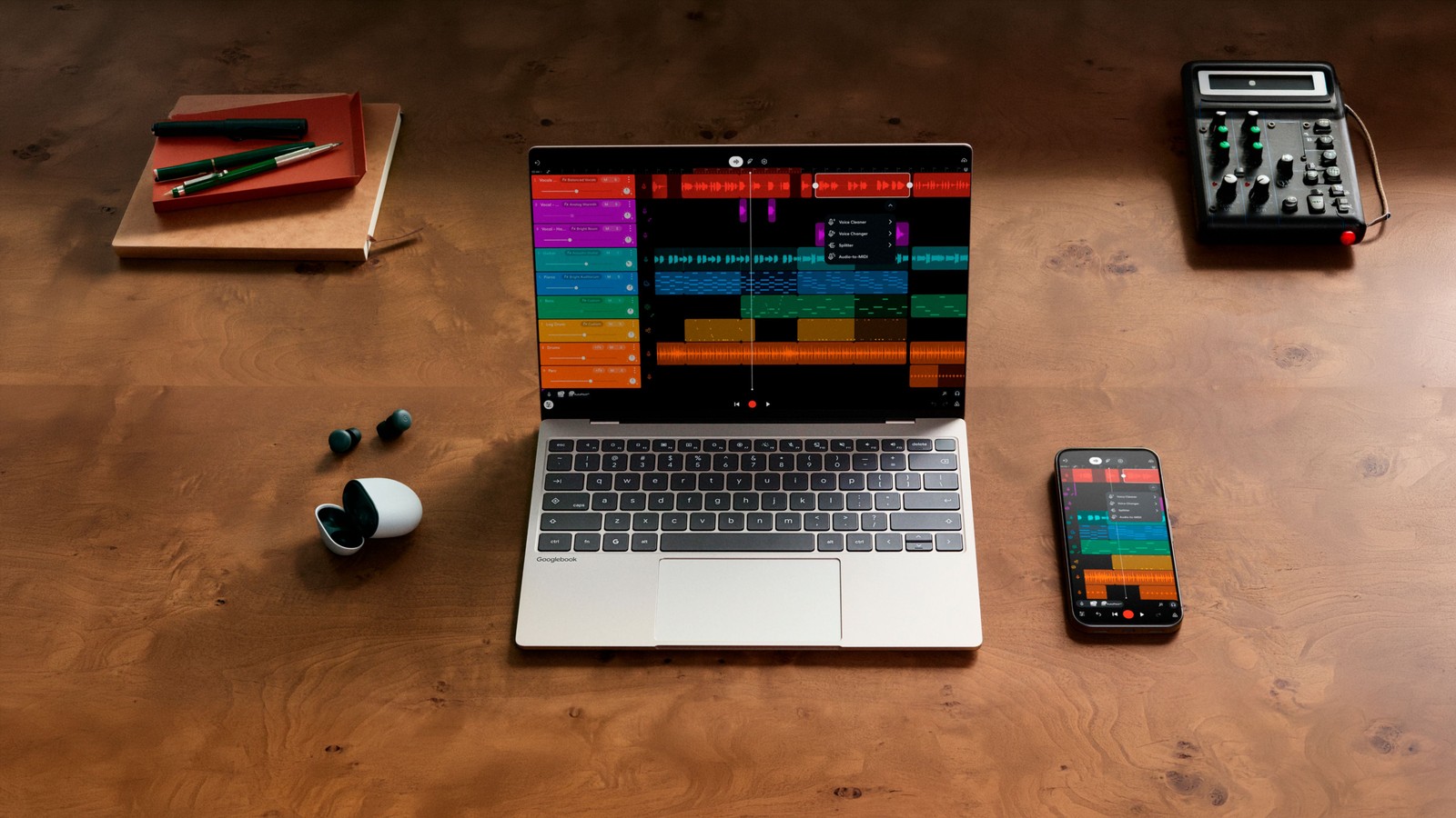 Googlebook com o app de edição de música aberto, ao lado de celular e fones