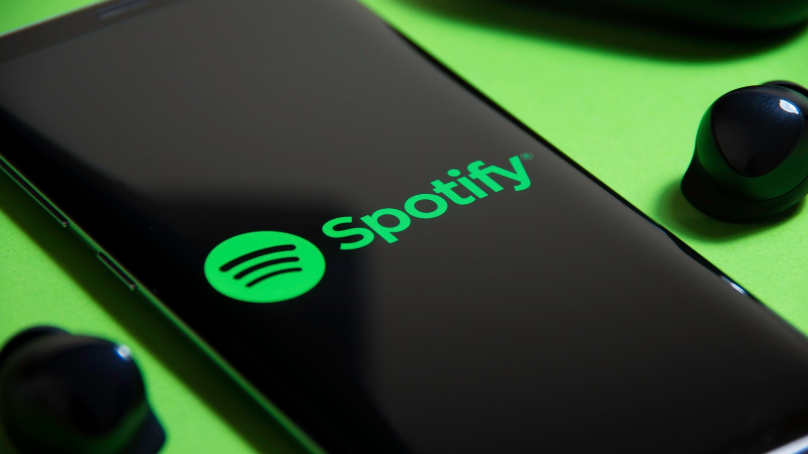 Aplicativo do Spotify aberto em um celular ao lado de fones sem fio