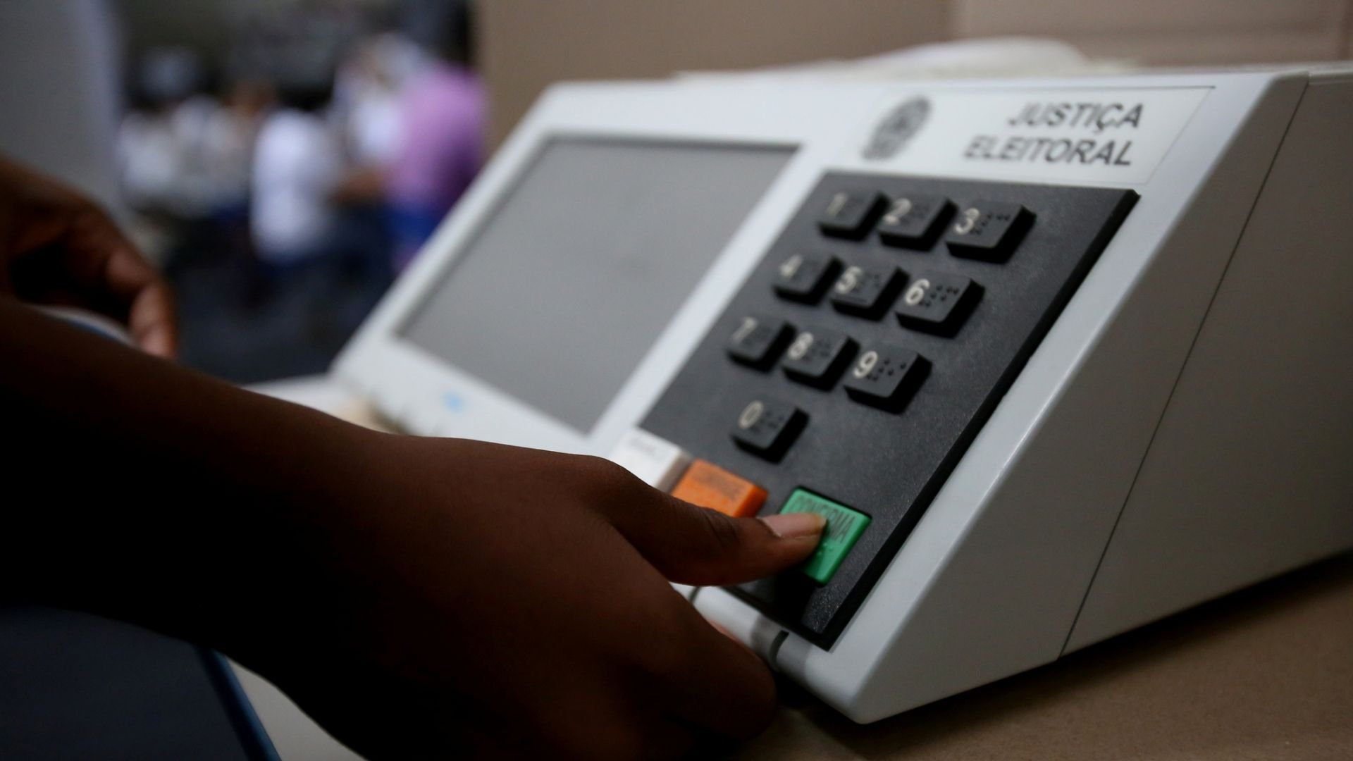 Mão de eleitor apertando a tecla verde de confirmação na urna eletrônica